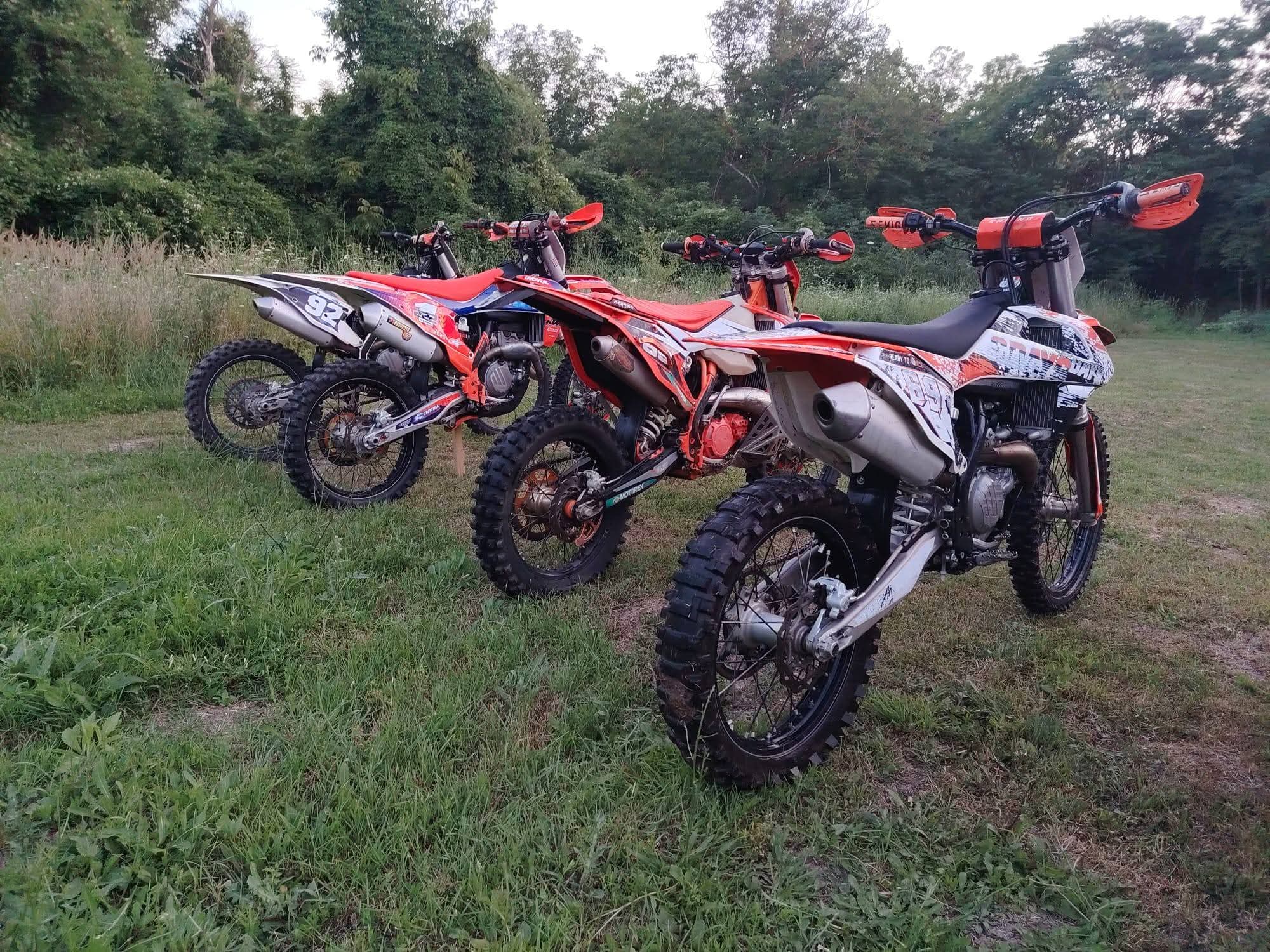 Row of KTM enduro bikes parked on a grassy field